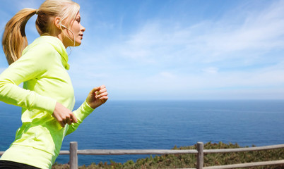 fitness, sport and healthy lifestyle concept - woman with earphones running and listening to music over sea background
