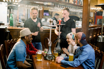 Fototapeta na wymiar Hookah smoking shisha in bar or nightclub, team of friends laugh, talk and drink beer.