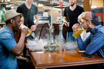 Hookah smoking shisha in bar or nightclub, team of friends laugh, talk and drink beer.