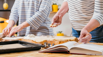 Homemade biscuits. Cropped shot of women working with dough, reading recipe in cookery book.