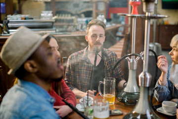 The company of diverse friends smoke hookah. Smoke. The boys lets out a smoke. Tabaka. Hookah Club Show.
