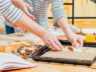 Gingerbread biscuits recipe. Closeup of female hands arranging fir tree shaped dough on sheet pan.