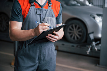 Close up view. Man at the workshop in uniform using notepad for his job for fixing broken car