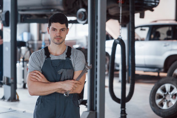 One person in the room. Portrait of serious worker in uniform that stands in his workshop with wrench in hand