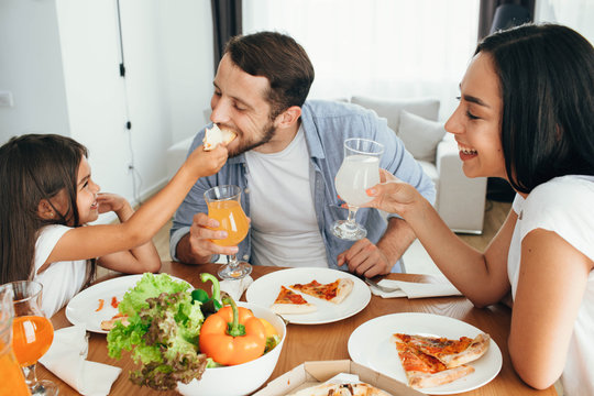 Family enjoying pizza lunch. Father, mother and daughter during dinner.Yammy, it's very tasty piece of pizza