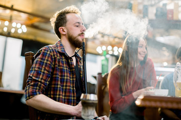 Rest in hookah, man makes tornado out of smoke shisha, his friends having fun and talking.