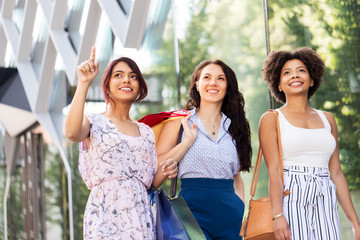 sale, consumerism and people concept - happy young women with shopping bags on city street looking up
