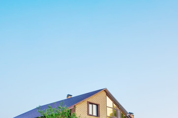 The roof of the house is pastel yellow and brown against a blue sky with light clouds. Bright sunny daylight. Place for text, minimalism. The concept of building houses, cottages. Copy space