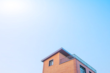 The roof of the house is pastel yellow and brown against a blue sky with light clouds. Bright sunny daylight. Place for text, minimalism. The concept of building houses, cottages. Copy space