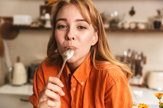 Happy cheerful young blonde girl chef at the kitchen holding tablespoon.