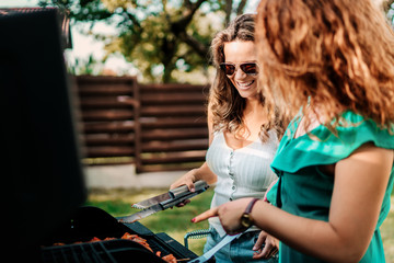 Fototapeta na wymiar Two female friends cooking on barbeque grill, having lunch in nature with friends