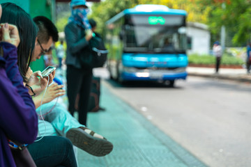 Asian people use smartphone waiting for bus at bus stop