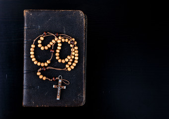 Rosary beads and prayer book on dark background.