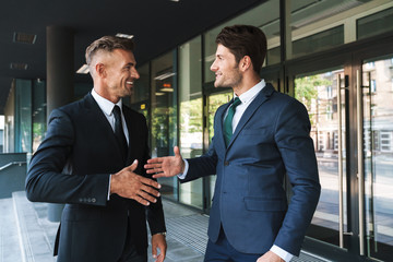 Portrait closeup of two joyful businessmen partners shaking hands outside job center during working...