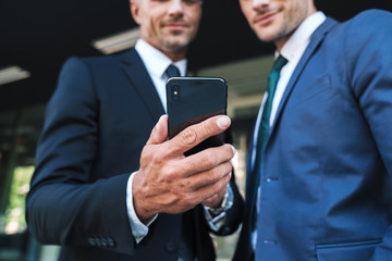 Portrait of handsome businessmen partners standing outside job center and using cellphone together during working meeting