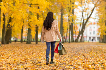 sale, consumerism, season and people concept - woman with shopping bags walking along autumn park