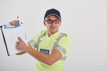 Showing part on the paper Policeman in green uniform and eyewear stands against white background in the studio with documents in hands