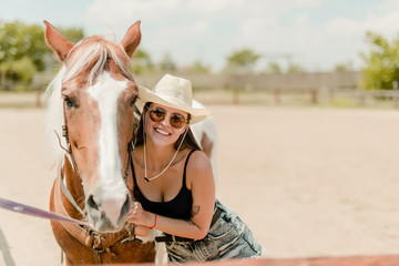 smiling country girl in cowboy hat with her horse on a ranch