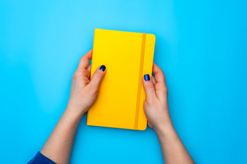 Beautiful female hands lie on a yellow diary