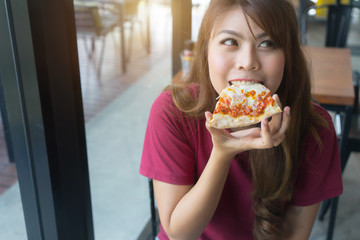 Happy asian girl eating tasty pizza at restaurant, close up..Young woman holding and bite sliced...