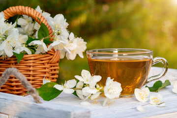 Fototapeta na wymiar Basket with Flowers of philadelphus somewhere called jasmine or mock orange and Cup with fragrant jasmine tea on a white wooden tray outdoors in summer, copyspace