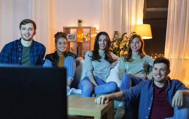 friendship, leisure, people and entertainment concept - happy friends watching tv at home in evening