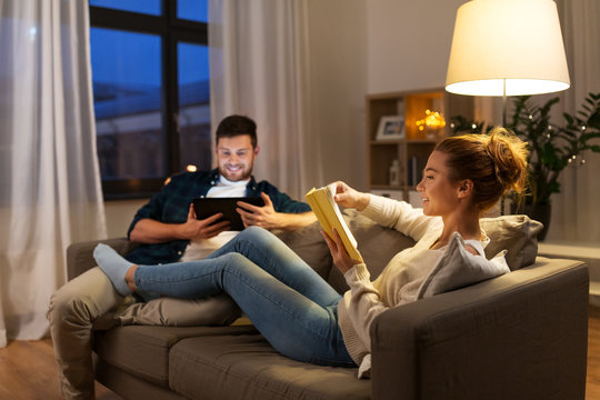 leisure and people concept - happy couple with tablet computer and book at home in evening