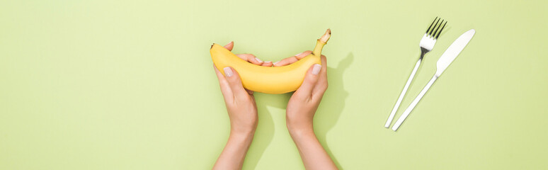 cropped view of woman holding banana in hands near fork and knife