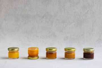 Five Small glass jar with metal cap with different kinds and colours of honey put in line, one upside down isolate and on grey cement background with copy space. Healthy product, natural. Horizontal
