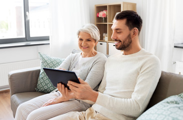 family, generation and technology concept - happy smiling senior mother and adult son with tablet computer at home
