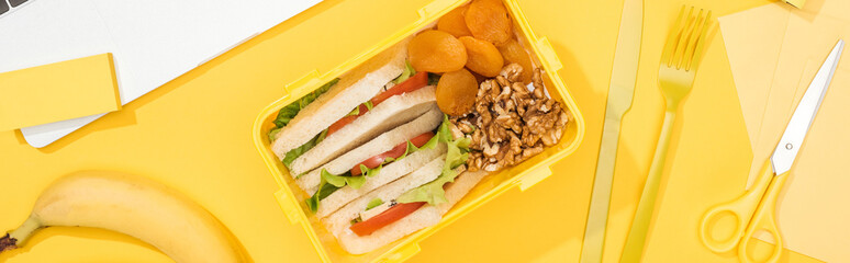 panoramic shot of lunch box with food near banana, knife and fork