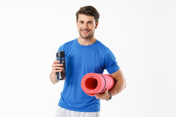Photo of handsome man wearing casual t-shirt smiling while carrying fitness mat and water bottle