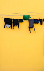 Dark laundry on clothes line with yellow wall at background on sunny day.