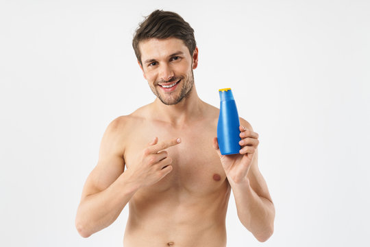 Photo closeup of caucasian naked man smiling and holding shampoo bottle while having shower