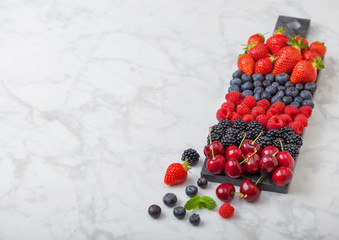 Naklejka na ściany i meble Fresh organic summer berries mix on black marble board on marble background. Raspberries, strawberries, blueberries, blackberries and cherries. Space for text