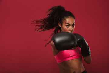 Serious strong young african sports woman boxer posing isolated over red wall background make...