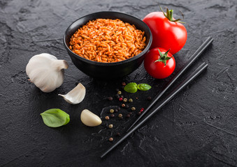 Black plate bowl of rice with tomato and basil and garlic and chopsticks on black stone background. Traditional food.