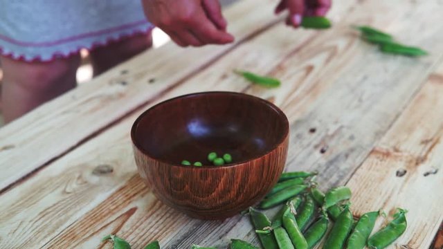 closeup of woman hand depod green peas in brown dish, on wooden table.