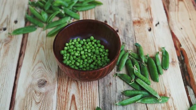 closeup of woman hand depod green peas in brown dish, on wooden table.