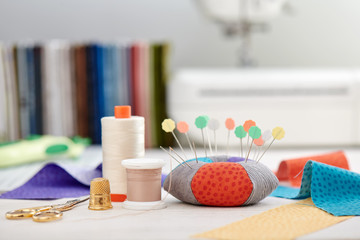 Pin cushion, brightly colored strips of fabric, sewing accessories  on the background of stack of...