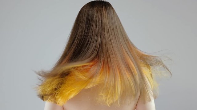 Video slow motion closeup portrait of a fashionable hairstyle of red-yellow in the studio on a gray background. Back view. Have a beautiful brunette beautiful loose colored hair fluttering