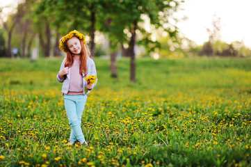 Obraz premium a little girl with red hair smiles against a field of dandelions and green grass. Summer, childhood, holidays. space for text, copy space