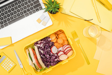 Fototapeta na wymiar top view of delicious lunch in box at workplace with yellow background