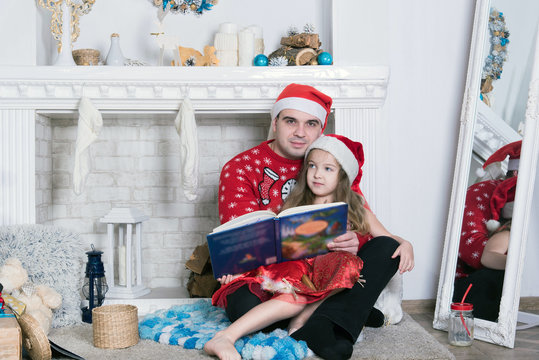 Merry Christmas and Happy Holidays! Xmas Christmas photo of surprised happy family. Little daugher hugging father. Reading book.