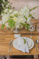 Flower arrangement with white flowers on a wooden table near the plate with devices
