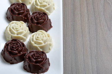 Chocolate coated sweets with almond filling. In the form of a flower. Lie on a white plate.