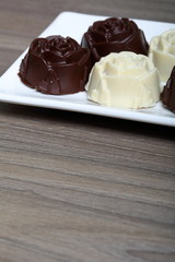 Chocolate coated sweets with almond filling. In the form of a flower. Lie on a white plate.