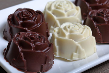 Chocolate coated sweets with almond filling. In the form of a flower. Lie on a white plate.