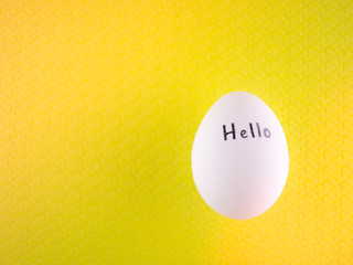 White chicken egg with black inscription hello on a yellow background.