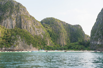 Traditional long tail boats, tourists, rocks and sea on and around Maya Bay beach in Koh Phi Phi Island, Krabi, Southern Thailand.